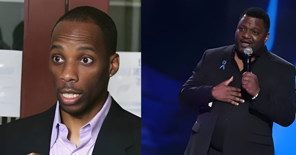 A man in a black suit stands on a stage holding a microphone and speaking into it.