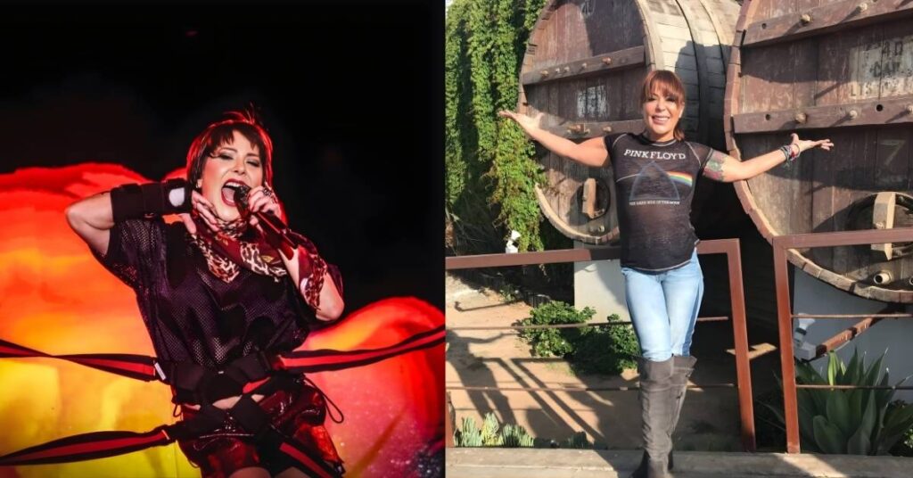 A performer wearing a mesh top, leopard print scarf, and shiny red shorts sings into a microphone on stage with a large, bright floral backdrop.