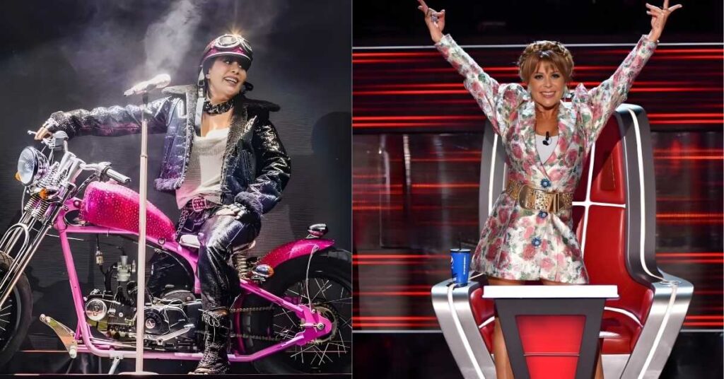 A person in a sparkly jacket and helmet sits on a pink motorcycle on a stage, holding a microphone.