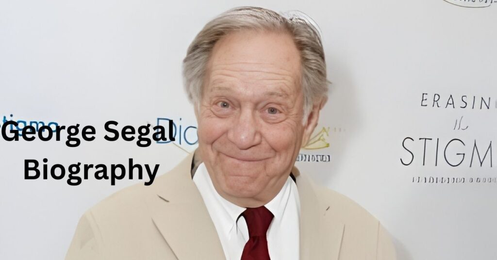 A person in a tan suit and red tie smiles in front of a wall of text.