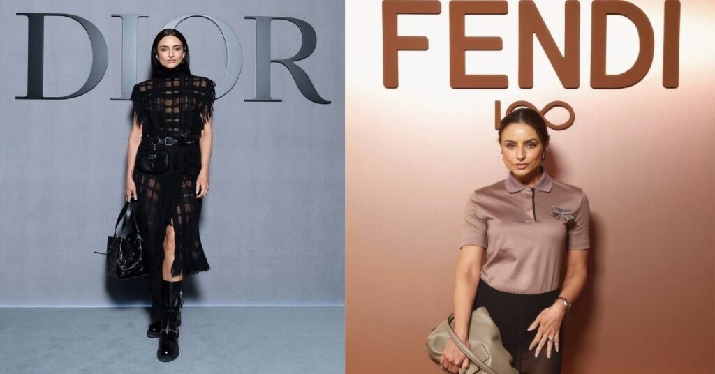 A person stands in front of a wall with FENDI 100 logo. The person wears a taupe collared shirt and a black skirt, holding a taupe handbag.