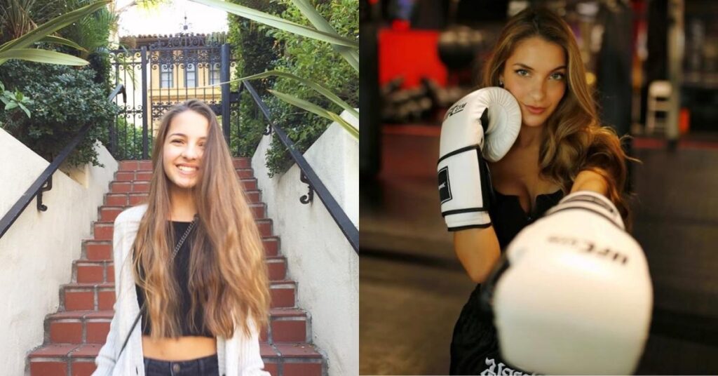 A person wearing white boxing gloves and black athletic shorts stands in a gym with punching bags in the background.