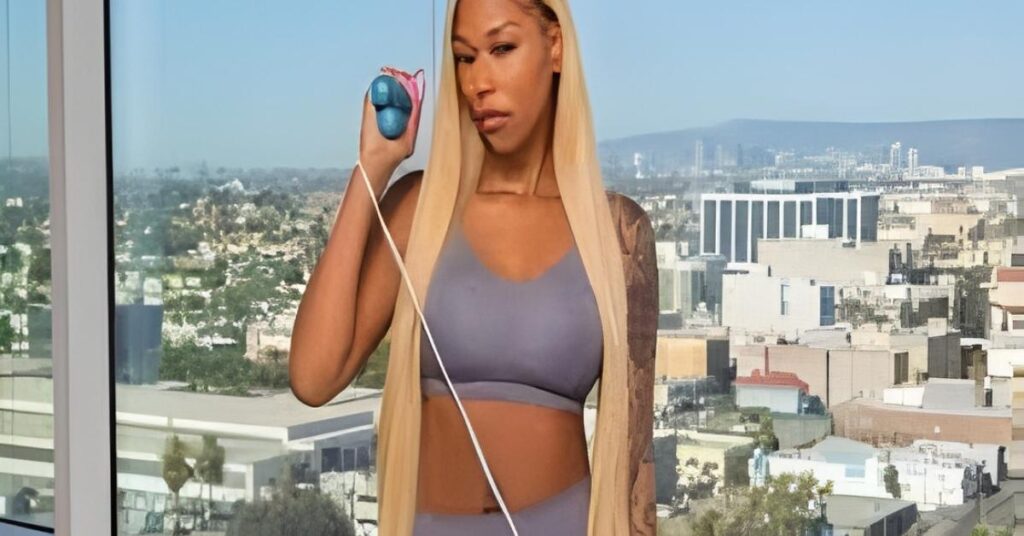 A person with blonde hair wearing a grey sports bra and leggings holds a jump rope with blue handles against a city skyline.