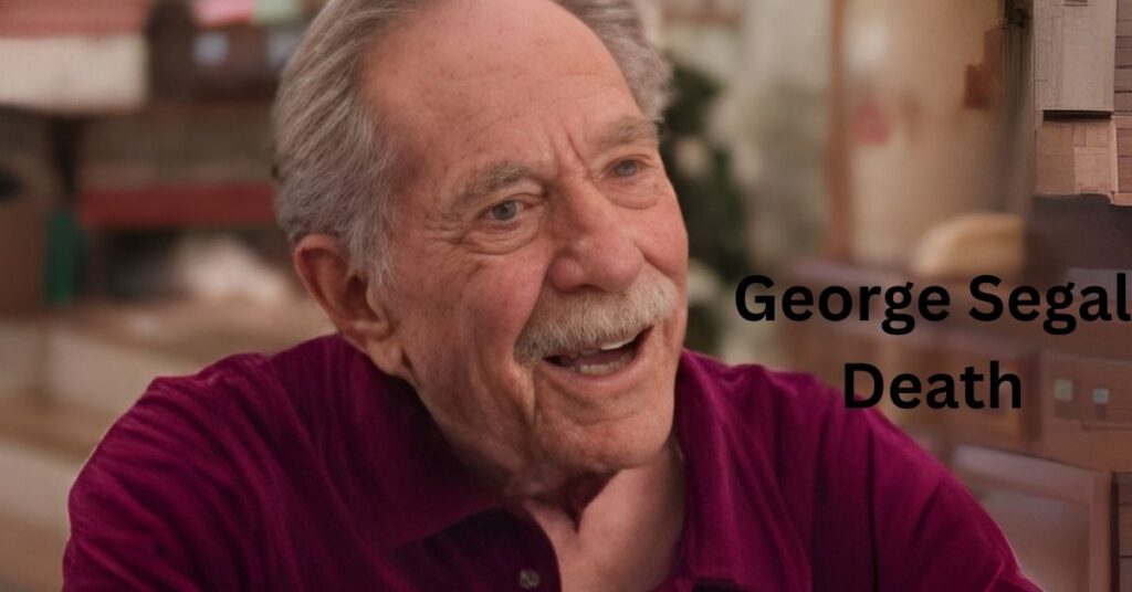 Person with gray hair and a mustache, wearing a red collared shirt, smiling.