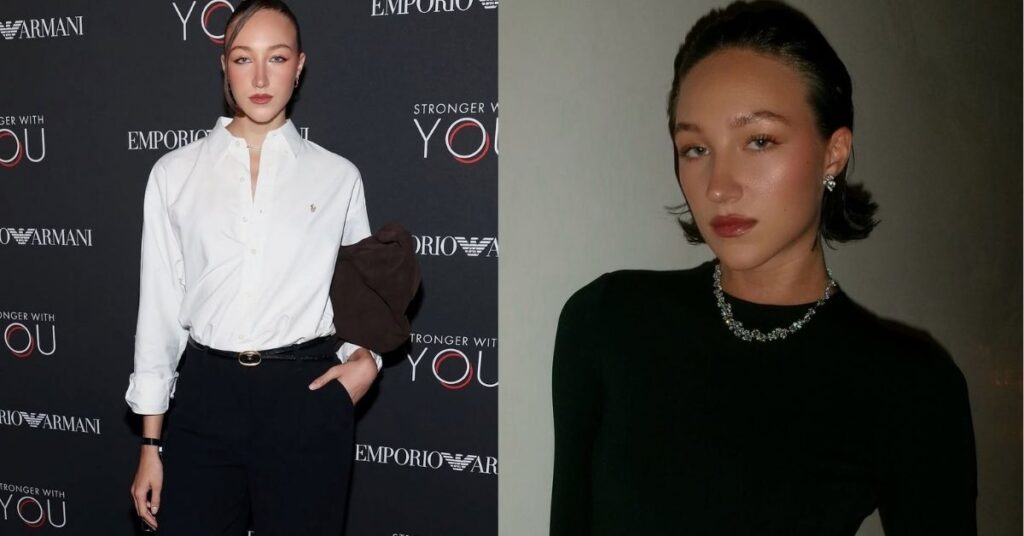 Ava Michelle stands in front of a dark backdrop with Emporio Armani and Stronger With You logos. They are wearing a white button-down shirt, black pants, and holding a brown garment over their arm