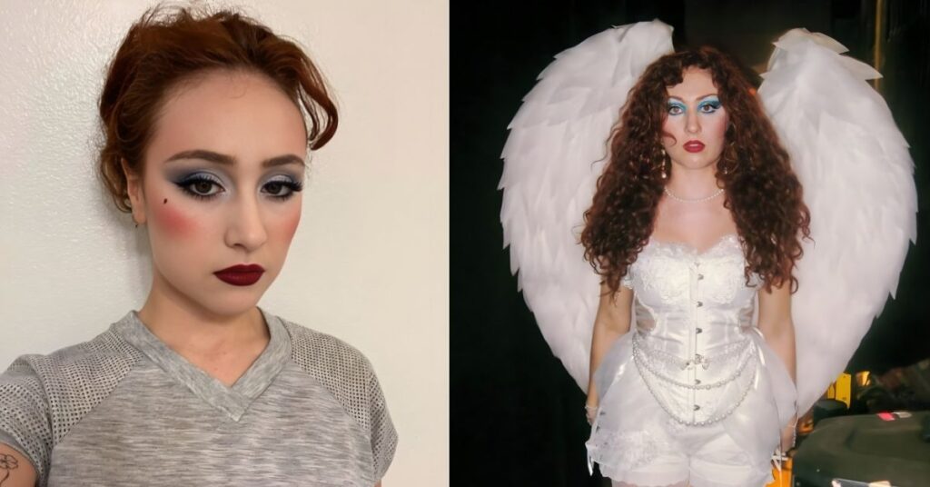 Chappell Rown, with curly red hair and dramatic blue eyeshadow, wears a white corset, ruffled shorts, and white stockings with bows, standing before large white wings.