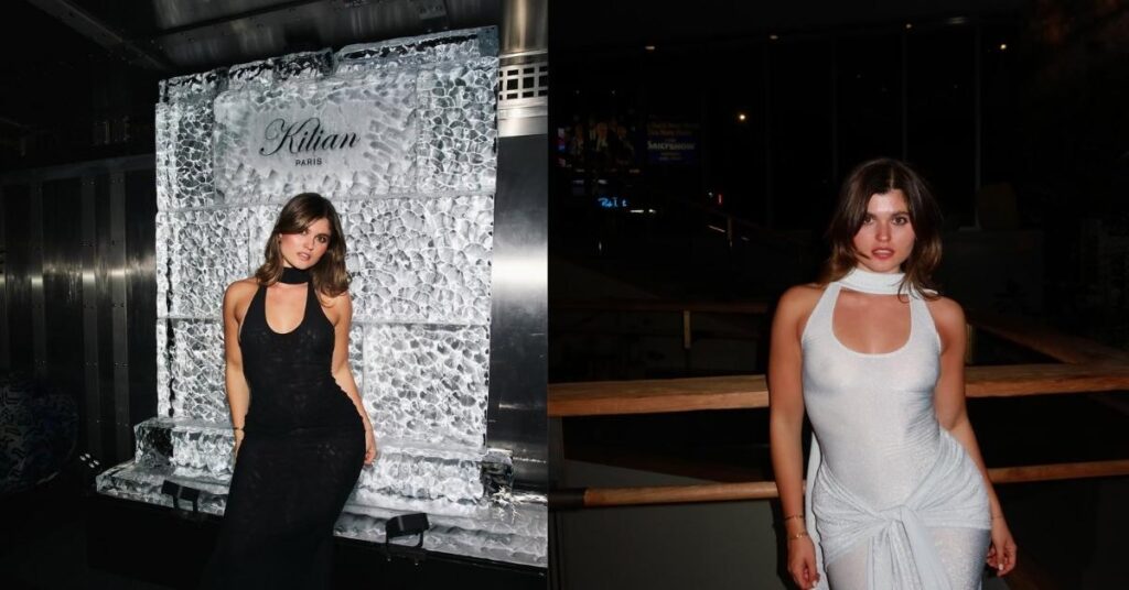 Elle Edwards stands on a wooden walkway at night wearing a sparkly white halter dress with a gathered waist and a scarf-like neckline.