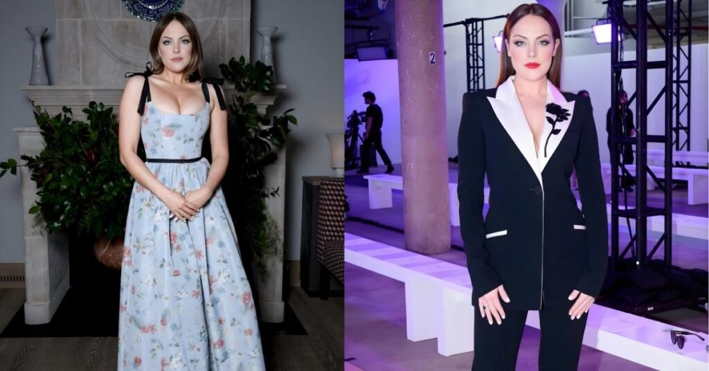 Elizabeth Gillies stands in front of a fireplace wearing a light blue floral print gown with black ribbon shoulder straps and a black belt.