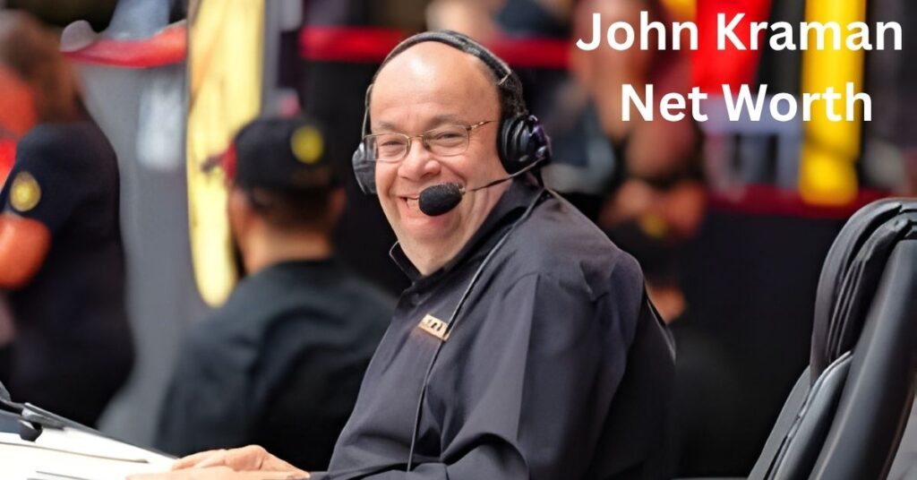 John Kraman, wearing a headset and glasses, smiles while sitting in a chair, with a blurred background of people and colorful lights.