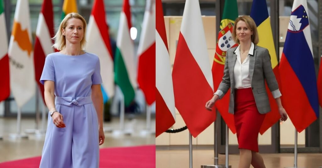 Kaja Kallas, in a light purple dress, walks on a red carpet with flags in the background.