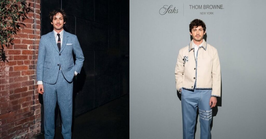 Logan Lerman stands in a light-blue tweed suit, white shirt, and striped tie, against a brick wall and dark paneling.