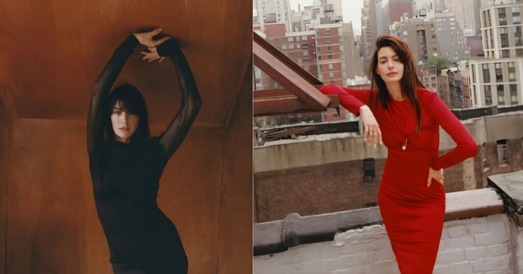 Anne Hathaway, in a black long-sleeved dress, stands with arms raised against a brown textured wall.