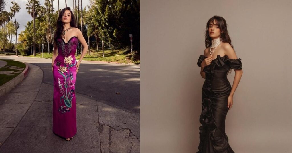 Camila Cabello, in a black off-the-shoulder ruffled gown with a pearl necklace, stands against a grey background.