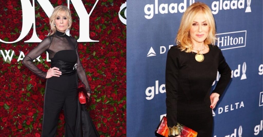 Judith Light, in a black jumpsuit with sheer sleeves and a long black train, stands on a red carpet in front of a wall of red roses.