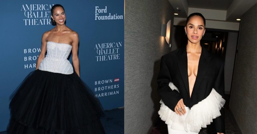 Misty Copeland is wearing a black oversized blazer over a white gown with ruffled detailing, standing in a hallway.