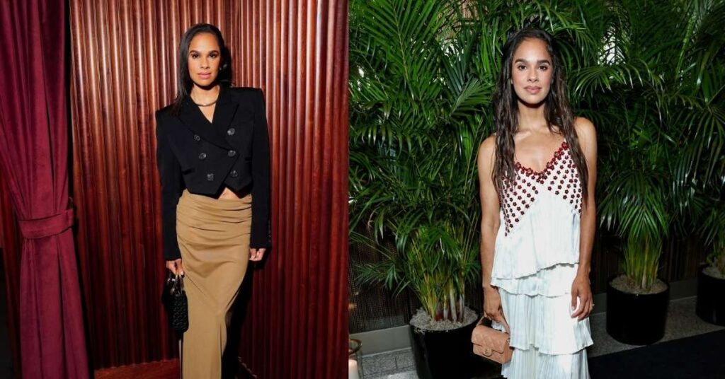 Misty Copeland stands in a black, cropped double-breasted blazer over a tan draped skirt, holding a black purse.