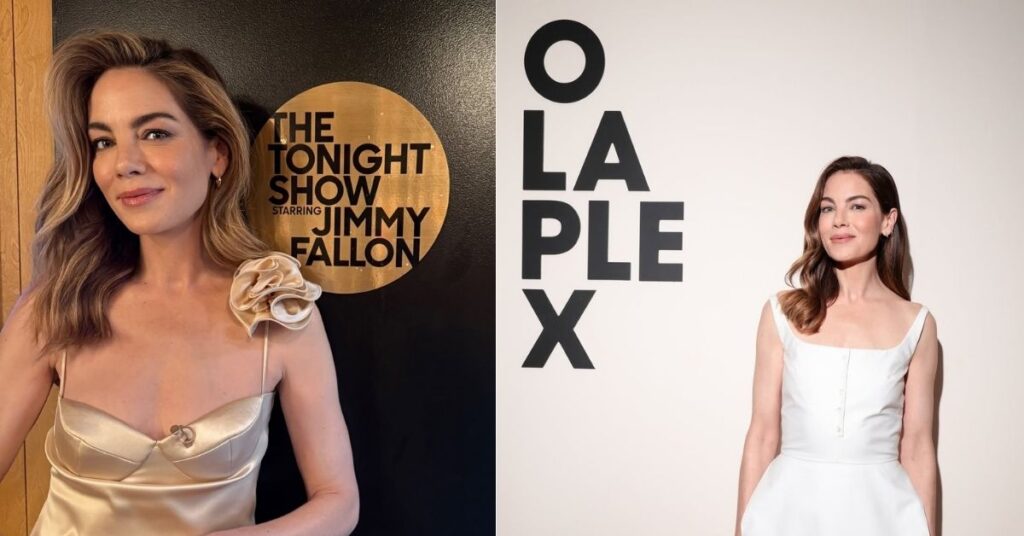 Michelle Monaghan, in a white sleeveless dress, stands in front of a wall with OLAPLEX in large black letters.