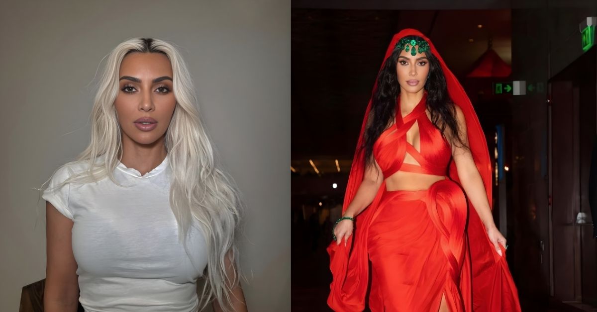 Kim Kardashian, in a flowing red dress and headscarf, adorned with green jewels, poses with one hand on their hip and the other holding the dress.
