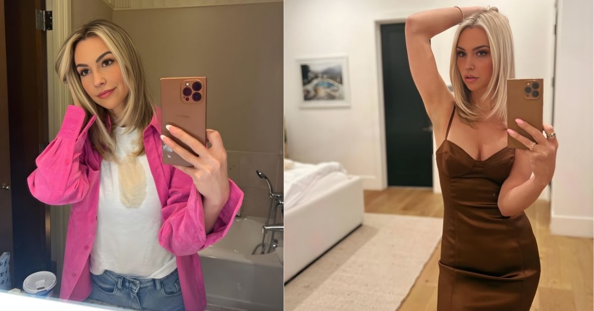 Lisa Stelly, in a brown satin slip dress, takes a selfie in a well-lit room with a modern chandelier and a bed in the background.