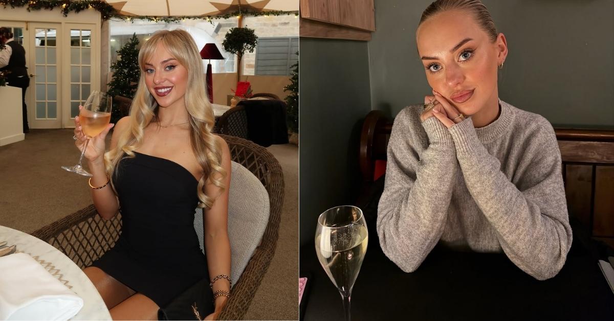 Rhiannon Blue wearing a gray sweater with hands clasped under their chin sits at a table with a glass of champagne.