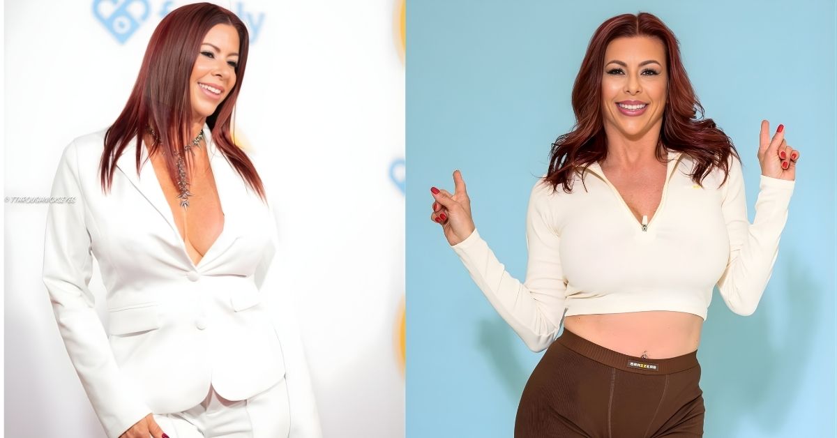 Alexis Fawx, with long, dark red hair, smiles while wearing a white suit and a decorative necklace.