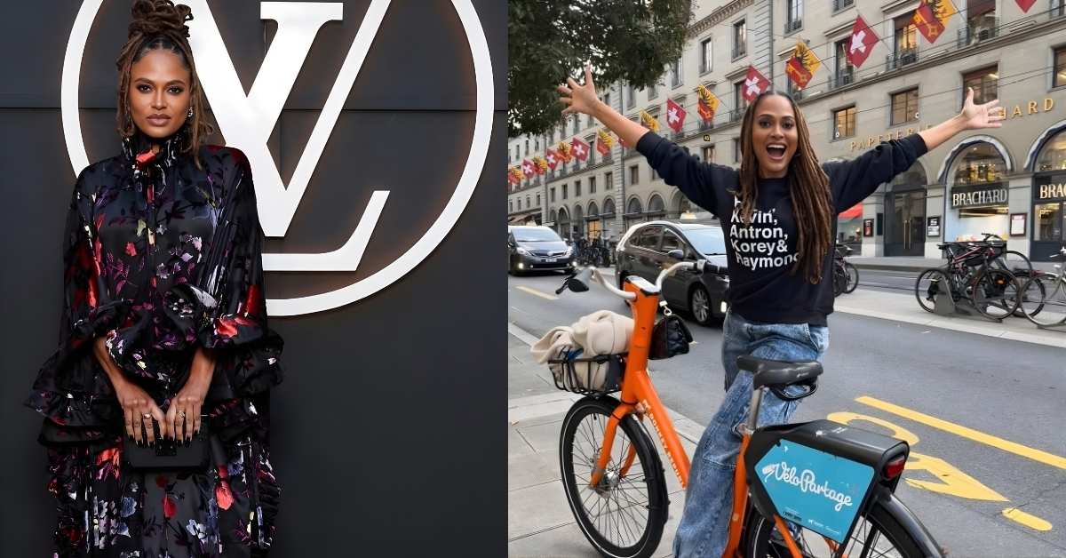 Ava DuVernay, with locs hairstyle and arms outstretched, sits on an orange bicycle in front of buildings adorned with Swiss flags.