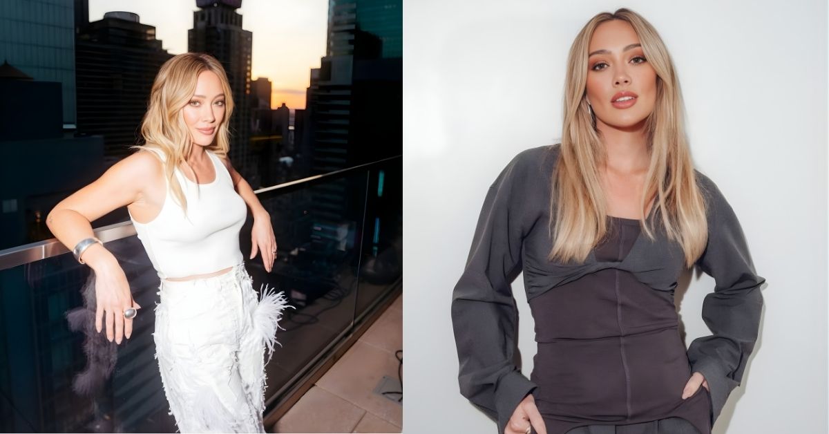 Hilary Duff, with blonde hair and makeup, wears a dark grey layered outfit, with her hands in their pockets, against a white background.