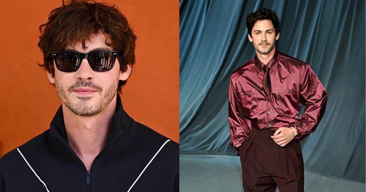 Logan Lerman, with dark hair, stands in front of a teal curtain, wearing a shiny burgundy button-down shirt, a matching tie, and dark burgundy pants.