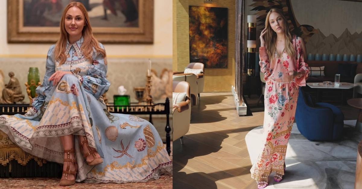 Meryem Uzerli is wearing a light blue dress with a seashell pattern sits on a couch in front of a painting.