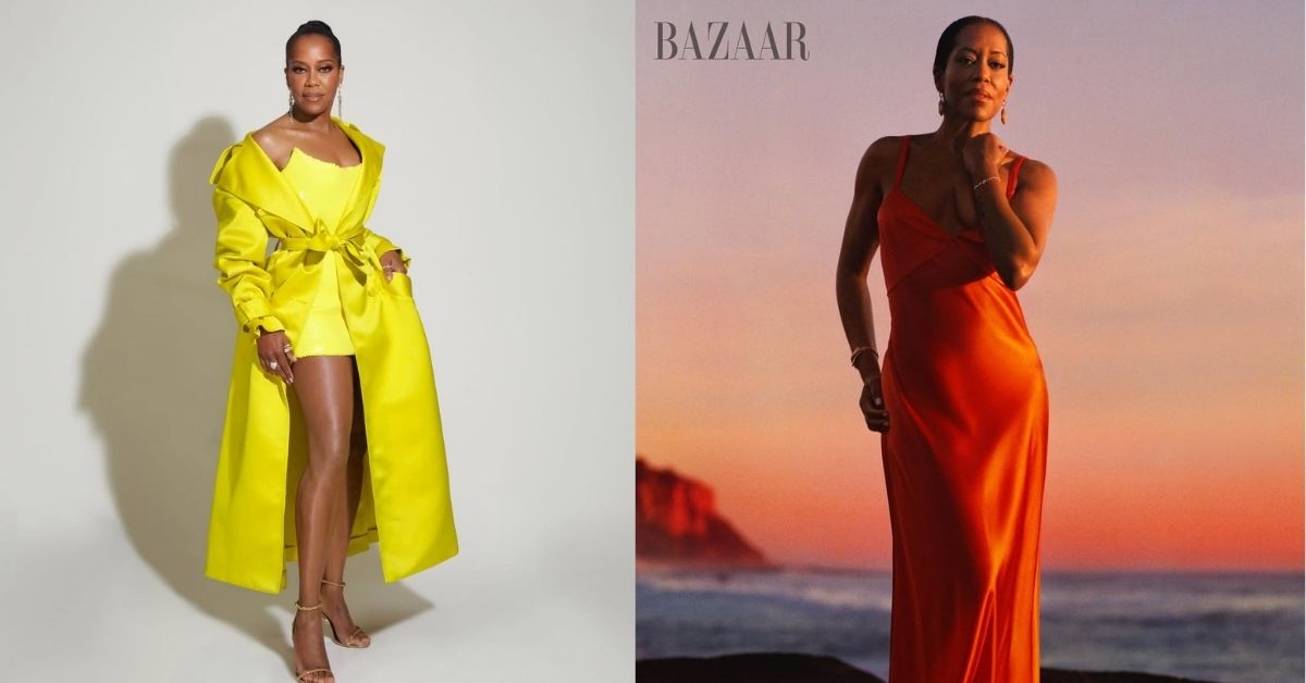 Regina King stands on rocks near the ocean wearing a long, flowing orange dress. The sunset casts a warm glow across the sky and the water.
