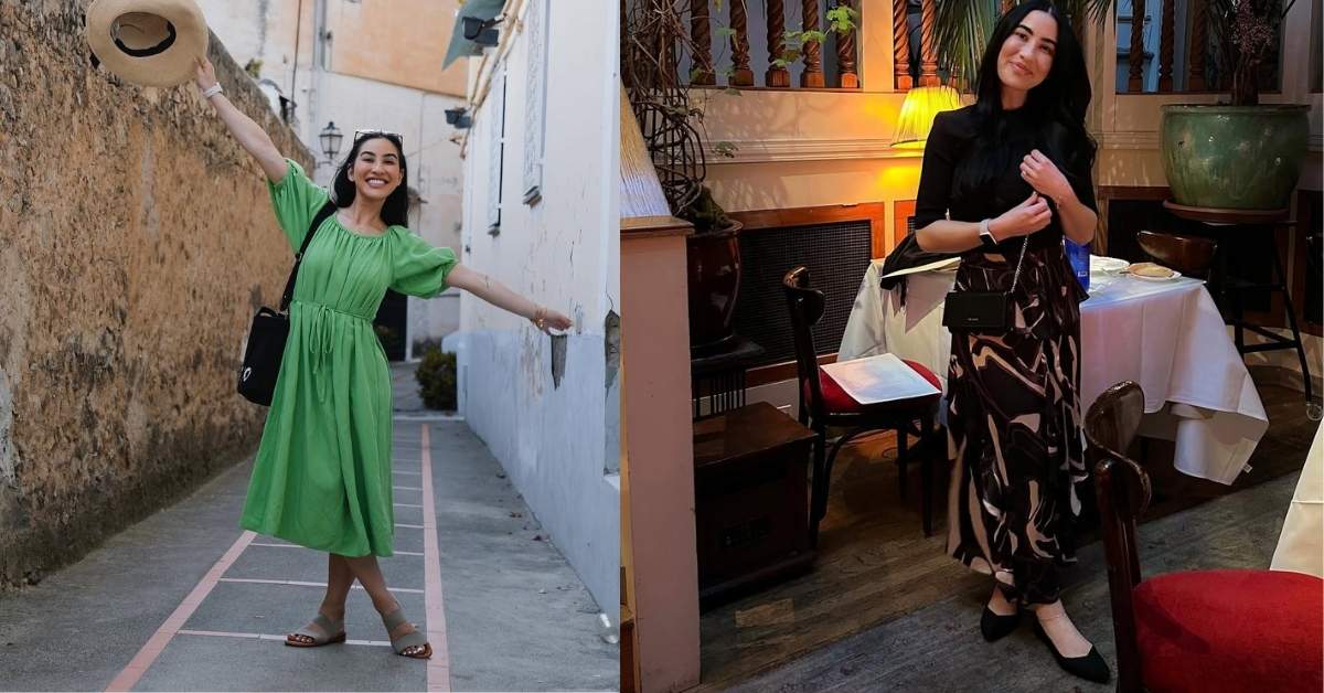Stephanie Buttermore, in a green dress, holds a straw hat above her head while standing in a narrow alleyway with stone walls.