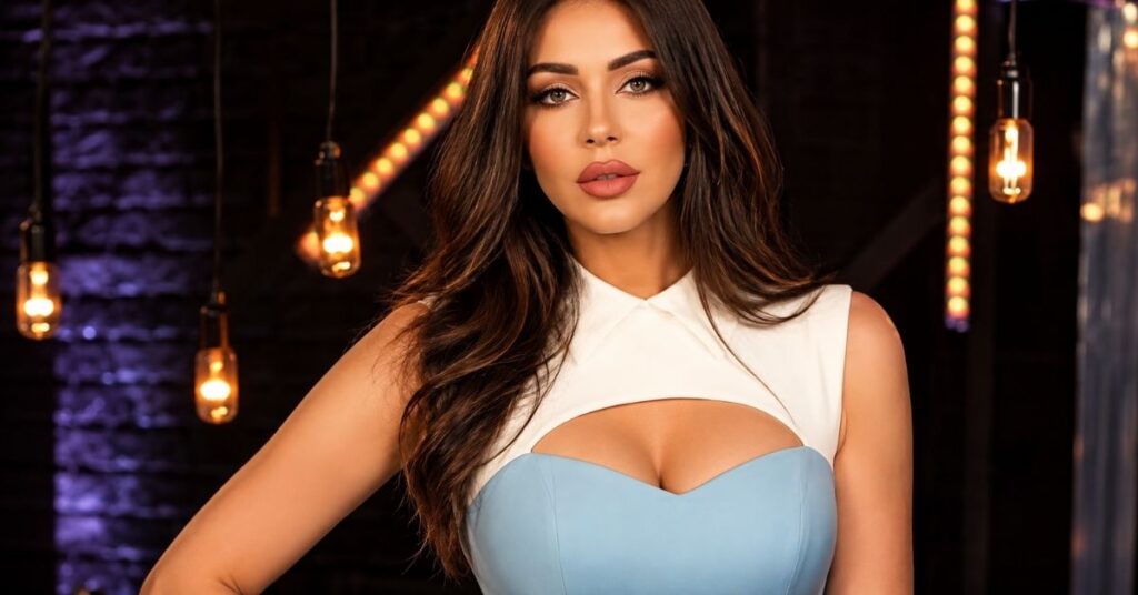 A person with long wavy dark hair poses in a sleeveless white top over a light-blue corset-style dress.