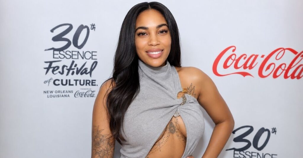 A woman with long dark hair smiles at a press backdrop for the 30th Essence Festival of Culture and Coca-Cola.